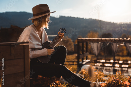 Fototapete Girl in cowboy hat playing ukulele sitting in home garden patio