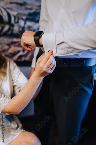 A woman  the bride cares  helps with her hand to fasten the cufflink on the groom s shirt  men with smart watches  wristwatches.
