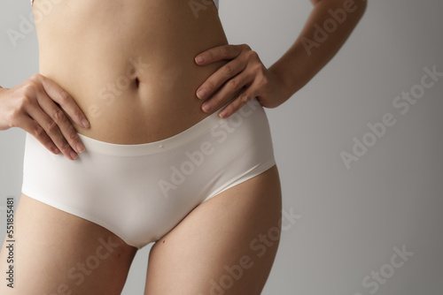 Close up asian female body wearing white high-waist panties over grey background.