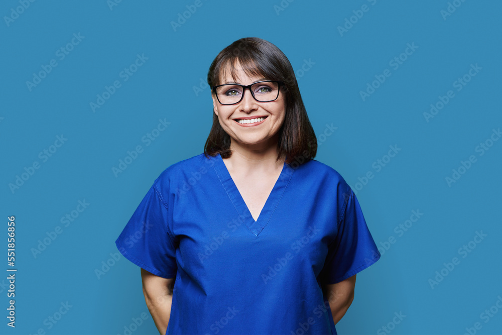 Smiling woman in blue scrubs uniform looking at camera on blue background Smiling woman in blue scrubs uniform looking at camera on blue background