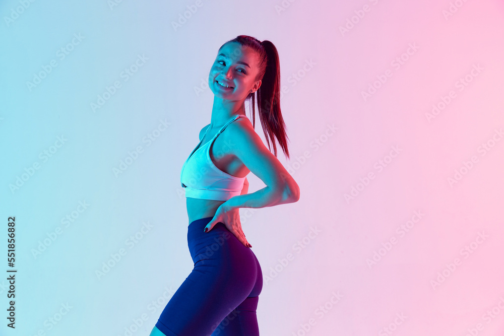 Portrait of young sportive woman in comfortable sportswear, smiling, posing isolated over gradient blue pink background in neon light. Concept of sport, fitness, health Portrait of young sportive woman in comfortable sportswear, smiling, posing isolated over gradient blue pink background in neon light. Concept of sport, fitness, health