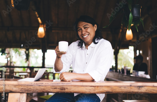 Cheerful ethnic man with cup of coffee in cafe