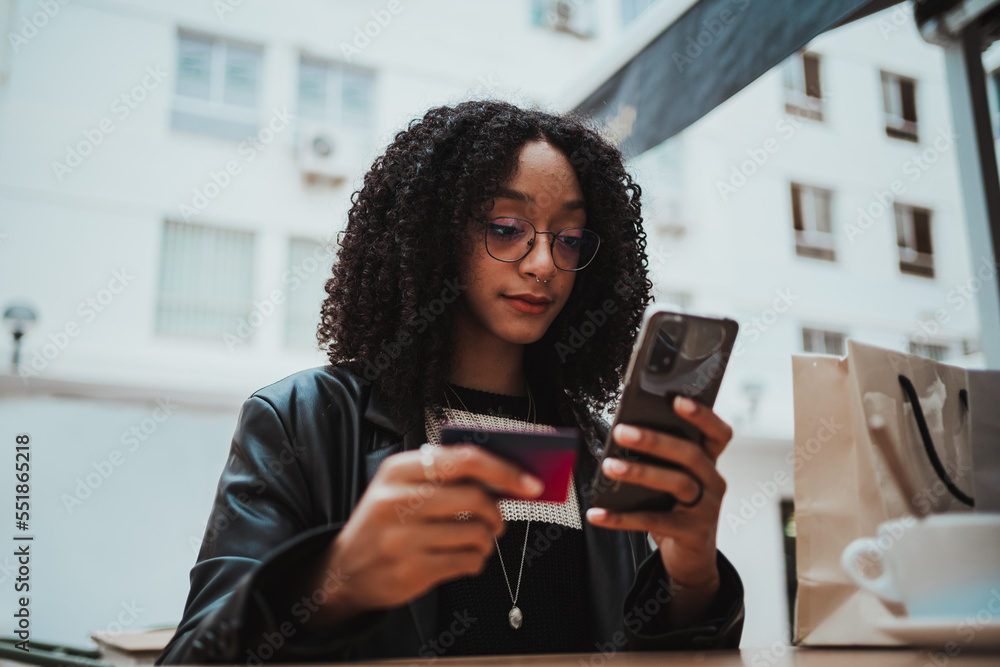African american girl paying online for a new dress. She is holding a credit card and her phone. African american girl paying online for a new dress. She is holding a credit card and her phone.