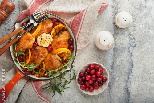 Baked chicken thighs with orange, cranberry and spicy herbs rosemary servered in frying pan on light background. Festive Christmas Dinner Concept menu. Top view. copy space