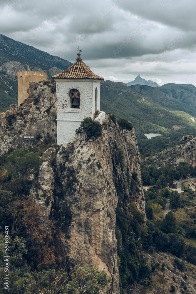 Aerial view of a religious bell tower perched on rocks in a mountain landscape