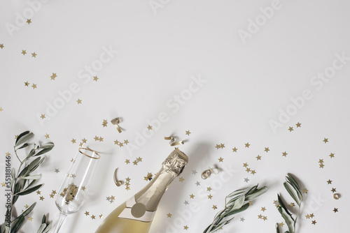 New Year festive web banner. Birthday, wedding party. Celebration concept. Champagne wine bottle, drinking glass. Olive tree branches. White table background. Golden star confetti. Flat lay, top view.