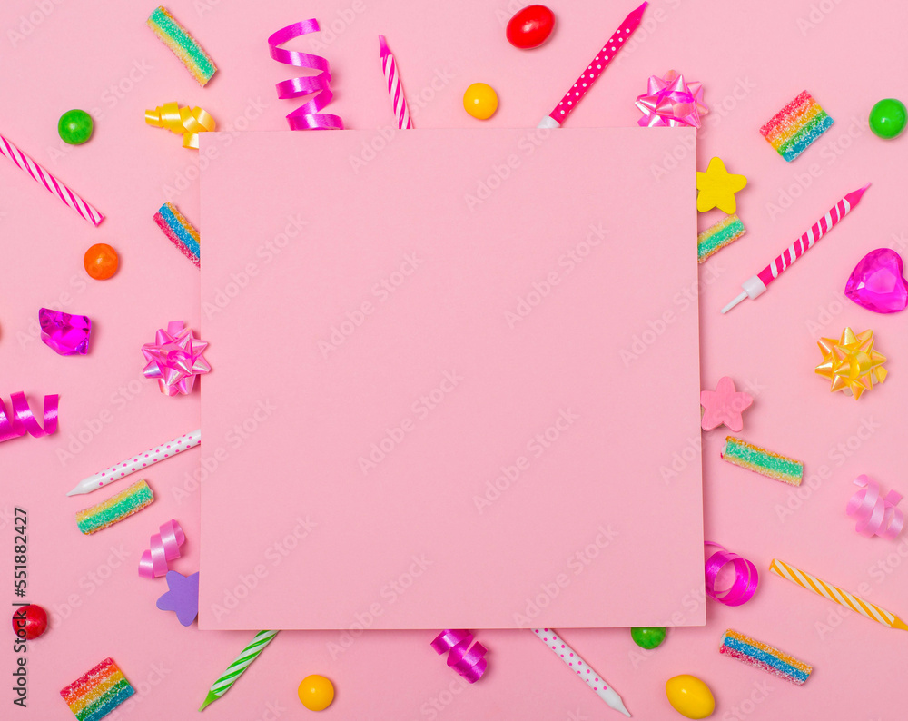 Children birthday party background with copy space paper on candels sweets cristals ribbons and confetti over pink background.