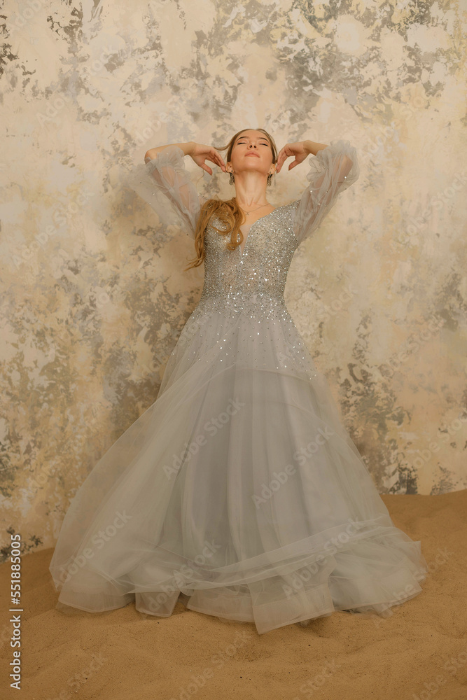 Fototapeta premium a girl in a dress on the sand against a shabby wall