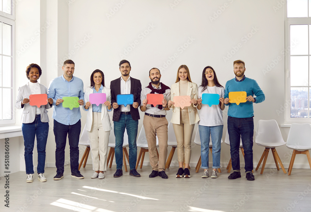 Different people sharing opinions. Happy diverse business team standing in office and holding colorful message bubbles. Group of employees showing red, green, purple, blue, yellow mock up word bubbles