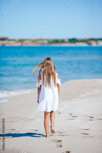 Back view of adorable little girl with long hair in white dress walking on tropical beach vacation © travnikovstudio
