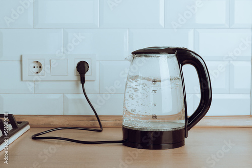 Transparent electric kettle with boiling water on the table in the kitchen.Kettle for boiling water and making tea and coffee.Home appliances for making hot drinks. photo