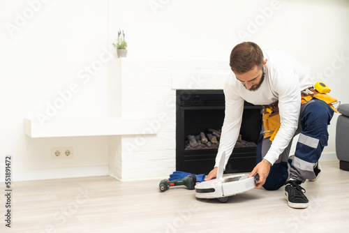 Robot vacuum cleaner repair. Man fixing robot vacuum cleaner DIY at home on the floor. Robotic vacuum cleaner maintenance and service. Smart device for easy housework. New tech for households.