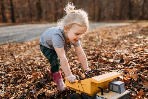 Happy child playing in fall leaves with toy truck