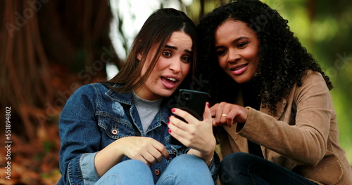 Diverse girls looking at cellphone screen. Woman calling friend to check out of content online