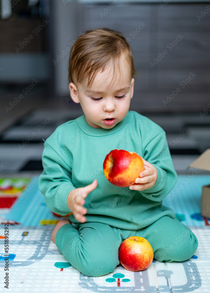 Fototapeta premium Cute baby boy eating apple at home. Healthy child nutrition