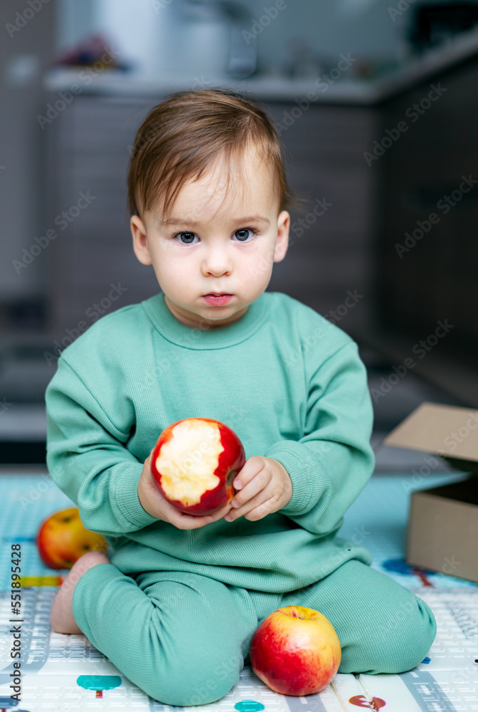 Fototapeta premium Cute baby boy eating apple at home. Healthy child nutrition