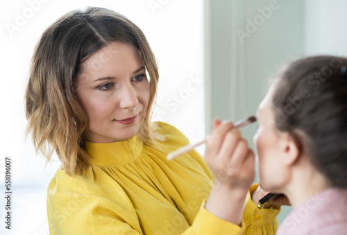 Beauty stylist applying make-up to a young model. Professional Make-up artist doing glamour