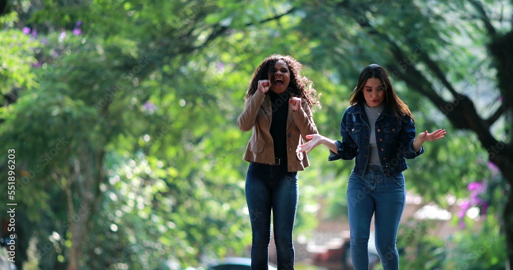 Excited two young women celebrating good news. Diverse girls dancing success