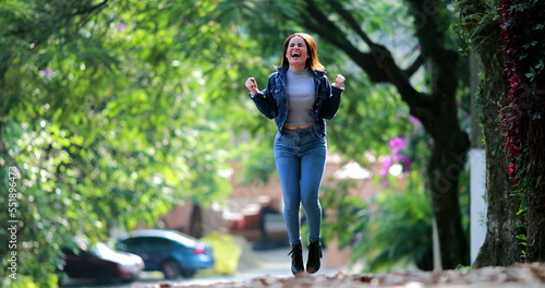 Excited girl jumping with joy outside. Young millennial woman in 20s celebrates