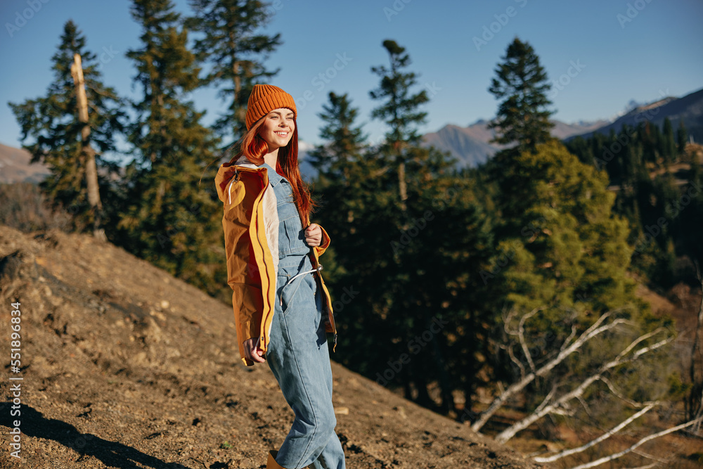 Naklejka premium Woman red hair on a hike in the mountains walking a smile and look at the view of nature autumn in a yellow raincoat and hat full-length happiness and freedom