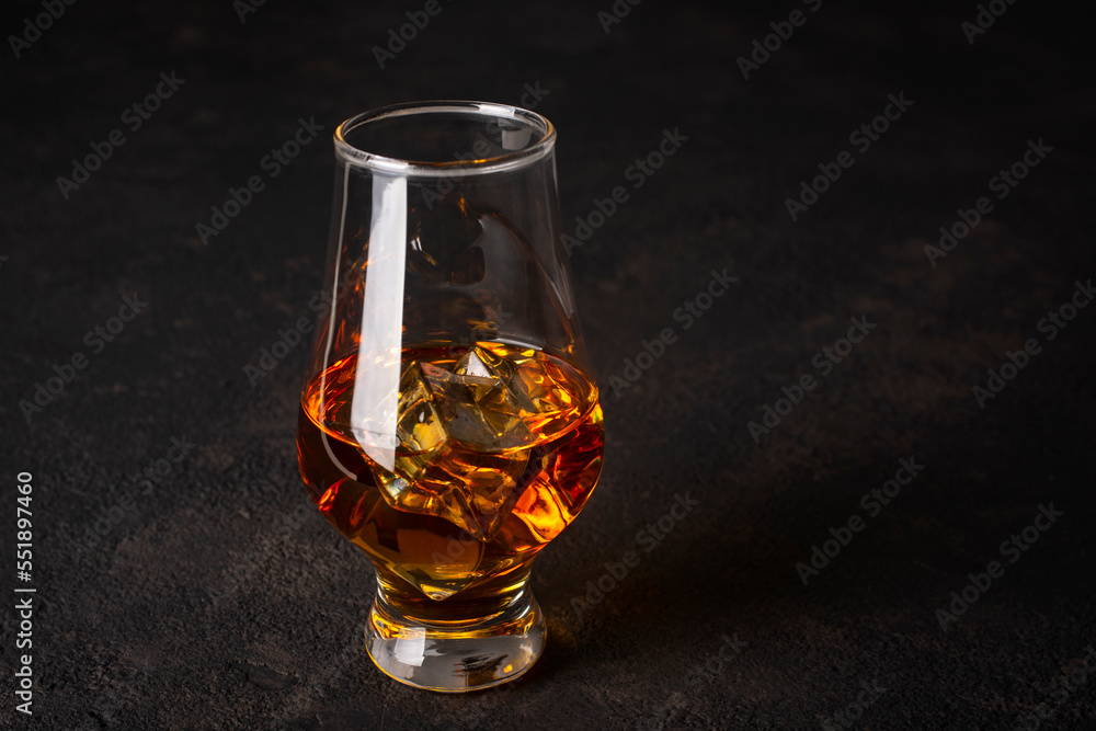Whiskey with ice in a glass on a dark background.