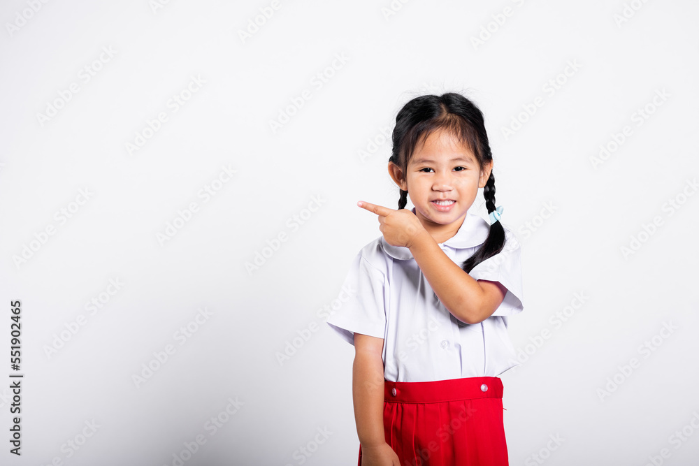 Asian toddler smiling happy wear student thai uniform red skirt keeps pointing finger at copy space in studio shot isolated on white background, Portrait little children girl preschool, Back to school Asian toddler smiling happy wear student thai uniform red skirt keeps pointing finger at copy space in studio shot isolated on white background, Portrait little children girl preschool, Back to school