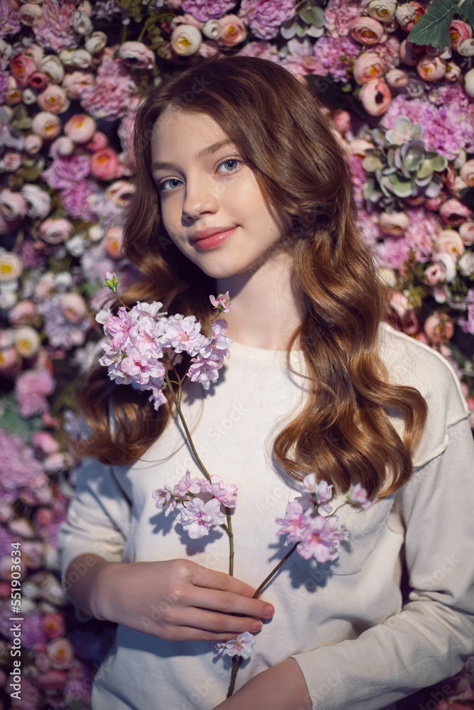 Naklejka premium portrait of a teenage girl with long hair in a white sweater against a wall of flowers.