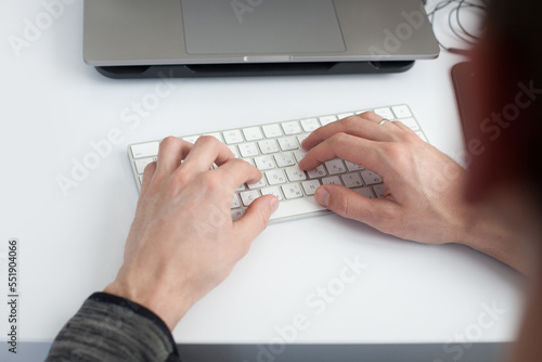 cropped shot of man typing with laptop at workplace on white surface