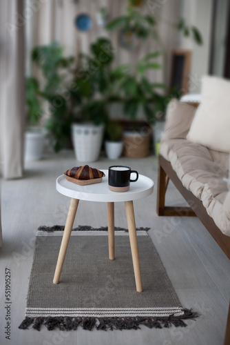 Table with croissant, cup and soft couch in light balcony room