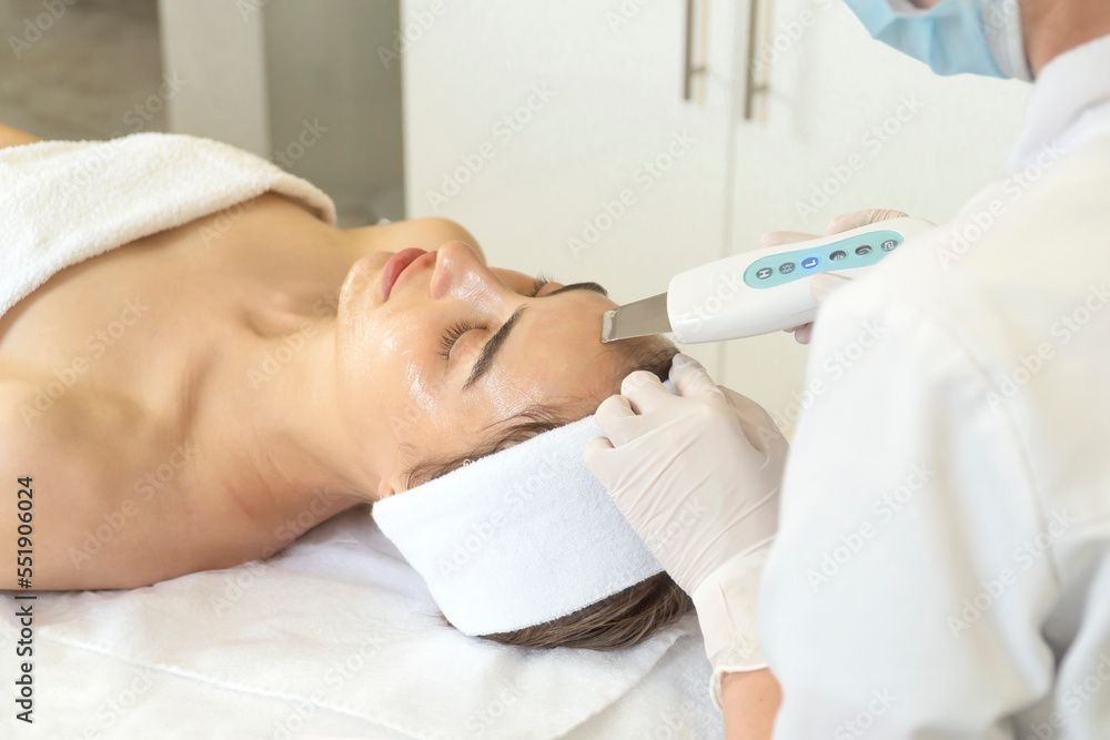 doctor cosmetologist makes a procedure for a beautiful brunette woman to a patient the procedure of cleaning the skin with an ultrasound machine. doctor cosmetologist makes a procedure for a beautiful brunette woman to a patient the procedure of cleaning the skin with an ultrasound machine.