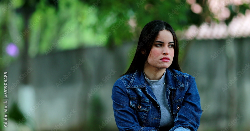 Pensive contemplative young woman sitting outside at park Pensive contemplative young woman sitting outside at park