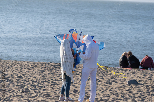 Two people preparing to fly a kite on the beach while two other people sit and talk 