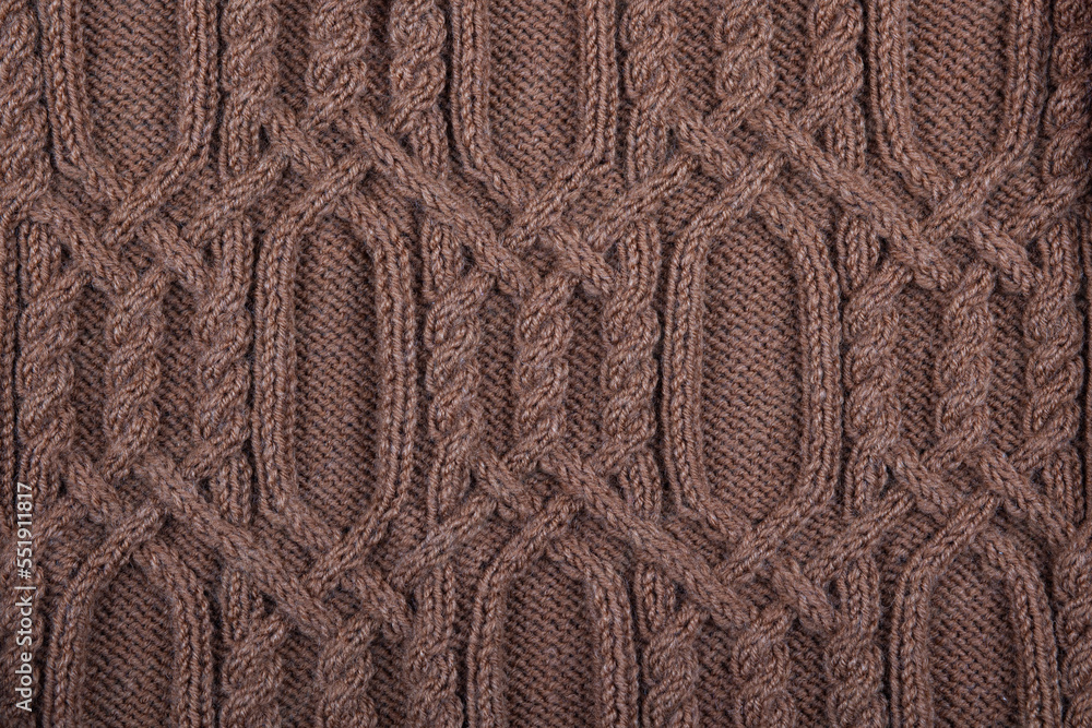 Knitted brown background. Large knitted fabric with a pattern. Close-up of a knitted blanket. Horizontal ornament.