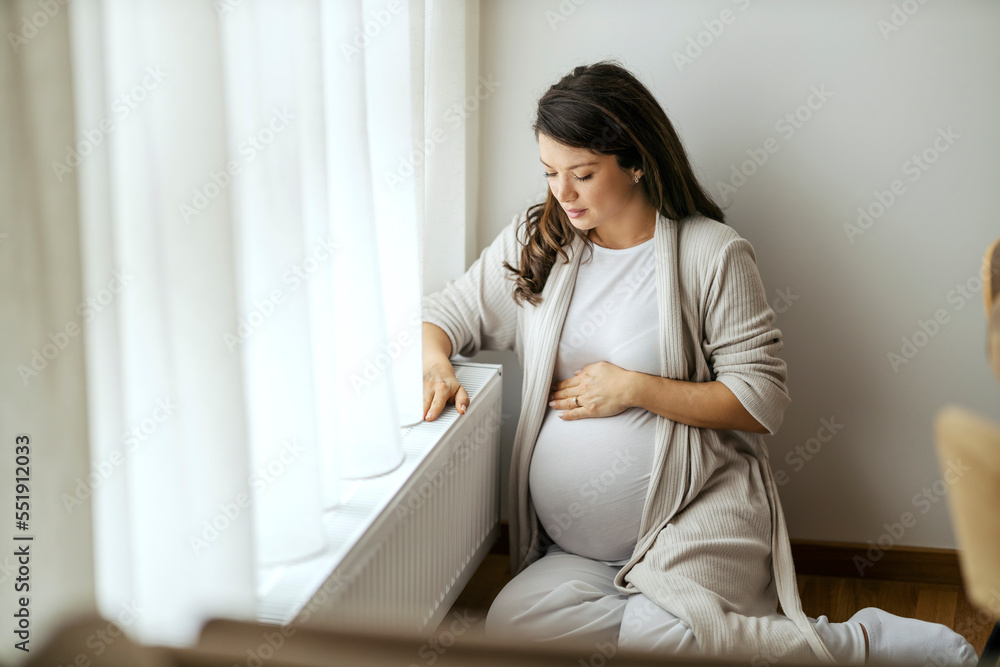A woman is sitting on a floor next to a cold radiator. A woman is sitting on a floor next to a cold radiator.