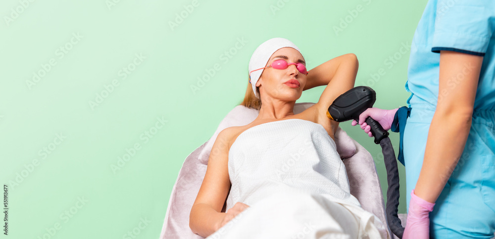 Banner of laser hair removal. Woman in eyeglasses at depilation procedure in beauty salon. Copy space. Beautician does an epilation on armpits. Concept of professional cosmetology Banner of laser hair removal. Woman in eyeglasses at depilation procedure in beauty salon. Copy space. Beautician does an epilation on armpits. Concept of professional cosmetology
