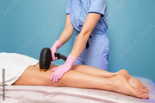 Professional cosmetologist in pink gloves does laser hair removal on woman's legs. The concept of salon care