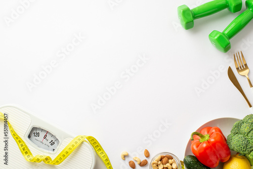 Weight loss concept. Top view photo of scales dumbbells tape measure plate with vegetables bell pepper cauliflower cucumber nuts and cutlery on isolated white background with copyspace