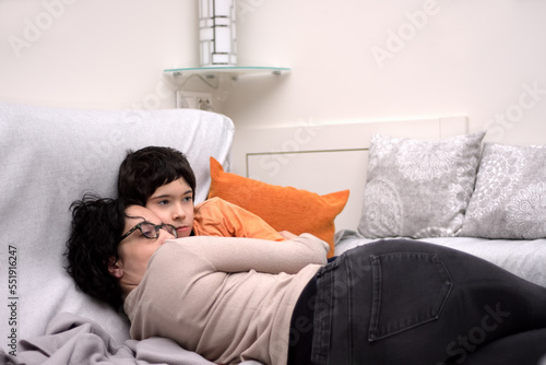 Young mother hugging with great affection and tenderness to her son, they are both lying on the sofa. Photograph in horizontal format. Photograph with space for copy space