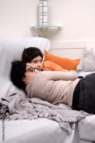 Young mother hugging with great affection and tenderness to her son, they are both lying on the sofa. Photograph in vertical format. Photograph with space for copy space