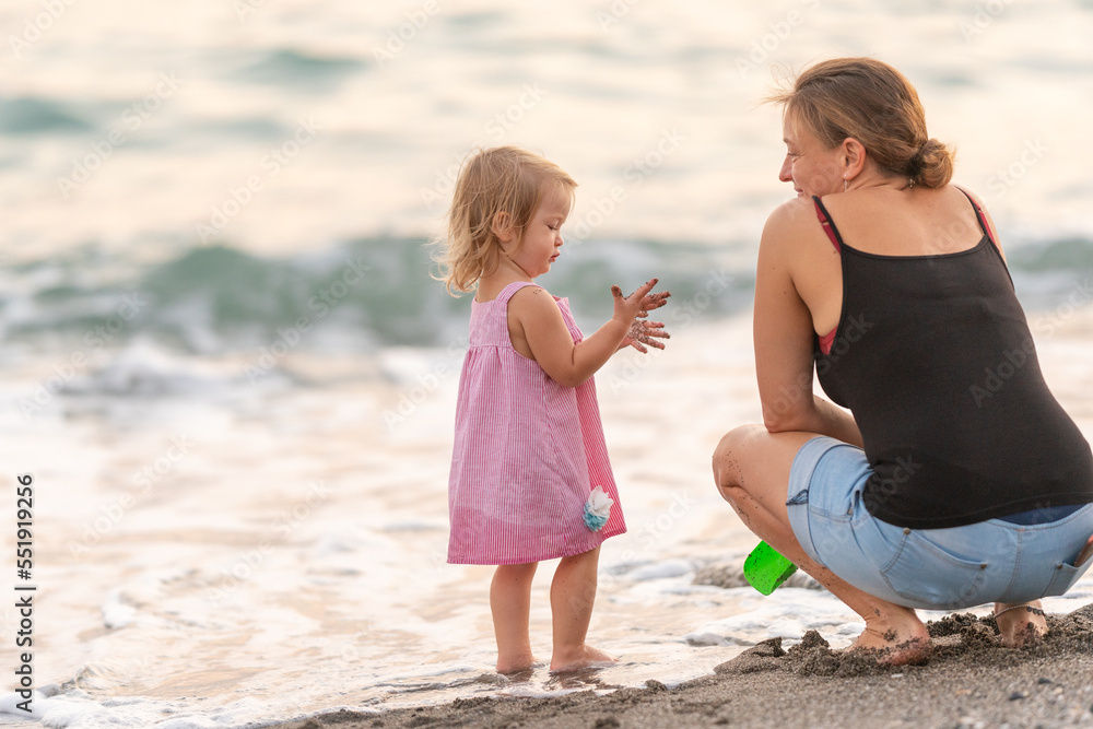 A joyful child frolics by the sea waves. Toddler in a pink dress talks with mother. Happy family vacation time A joyful child frolics by the sea waves. Toddler in a pink dress talks with mother. Happy family vacation time