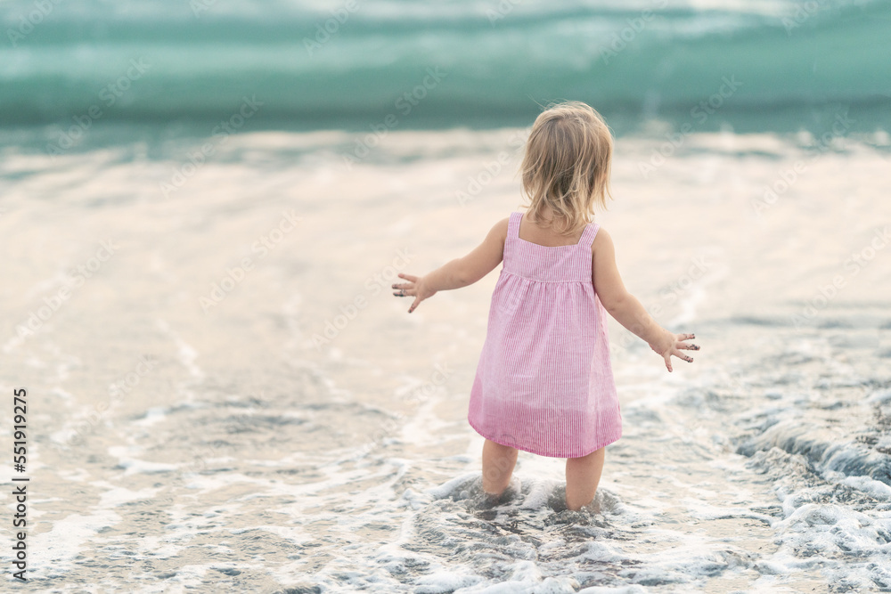 Little girl walking on sea. Toddler in a pink dress plays by the sea. Perfect day at the sea Little girl walking on sea. Toddler in a pink dress plays by the sea. Perfect day at the sea