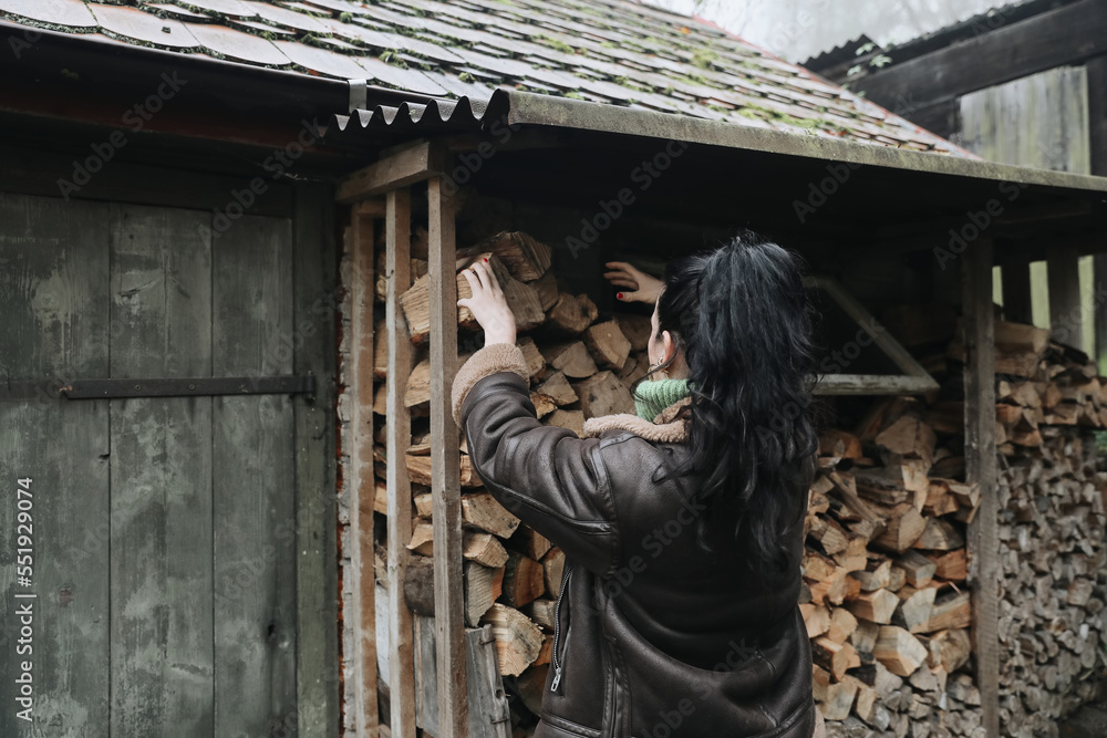 Young woman, girl holds firewood with her hands. Pile of stacked chopped wood prepared for heating the house. Collecting firewood for the winter, fire. Alternative energy source. Selective focus.