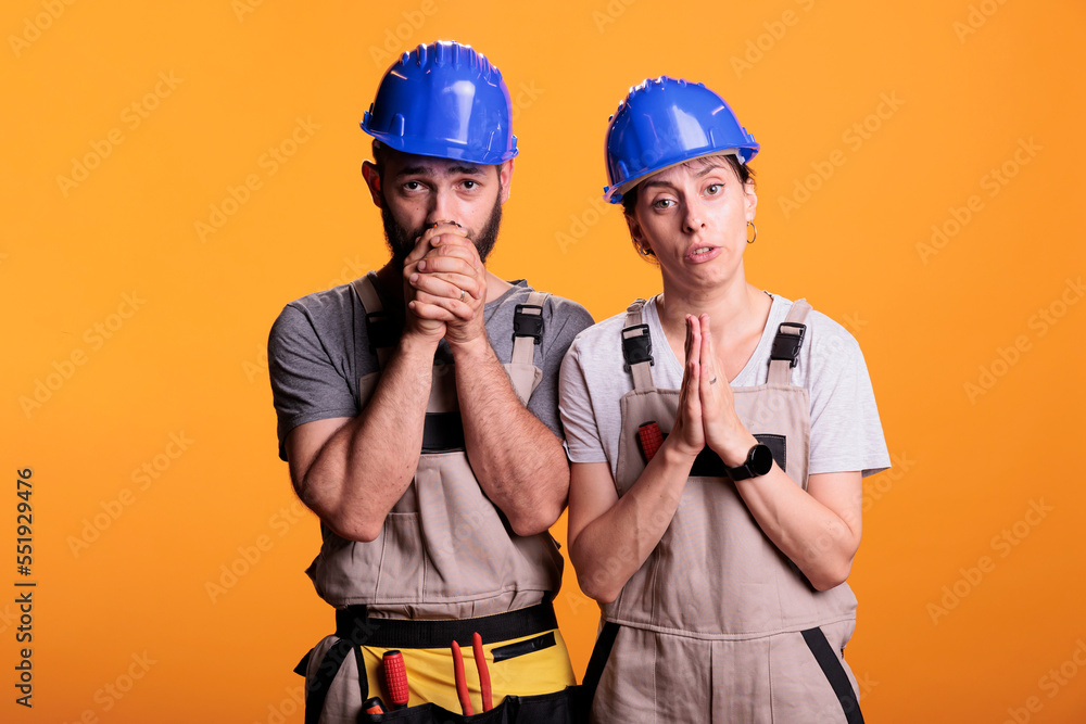 Professional renovators doing prayer hands on camera, begging and wishing for luck or fortune. Team of contractors praying, spiritual faithful builders standing over yellow background.