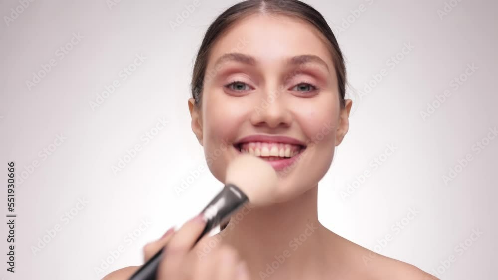 Cosmetic concept. Model doing make-up. Adoreble Girl runs a makeup brush over her face and touch camera. Young woman makes blush on the face using makeup brush. Slow motion. Cosmetic concept. Model doing make-up. Adoreble Girl runs a makeup brush over her face and touch camera. Young woman makes blush on the face using makeup brush. Slow motion.