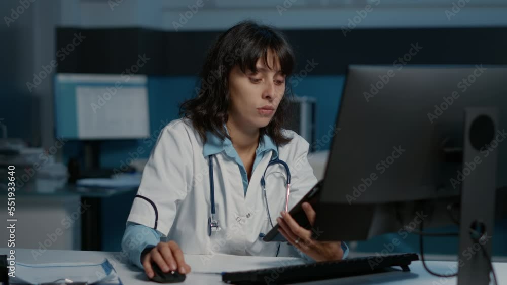 Physician doctor analyzing patient disease report on tablet typing medical expertise on computer while working late at night in hospital office. General practitioner planning health care treatment Physician doctor analyzing patient disease report on tablet typing medical expertise on computer while working late at night in hospital office. General practitioner planning health care treatment