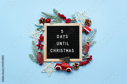 Felt letterboard with letters with countdown surrounded by winter seasonal decoration on blue background. 5 days until Christmas. Twenty-four day series of postcards. Selective focus