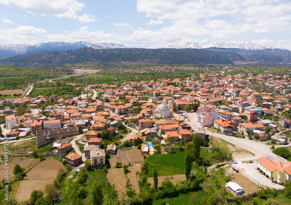 Aerial view of typical Turkish small town Yesildag of Burdur province on sunny spring day with snowy mountain range in background..