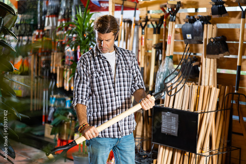 Attentive man choosing pitchfork in garden shop