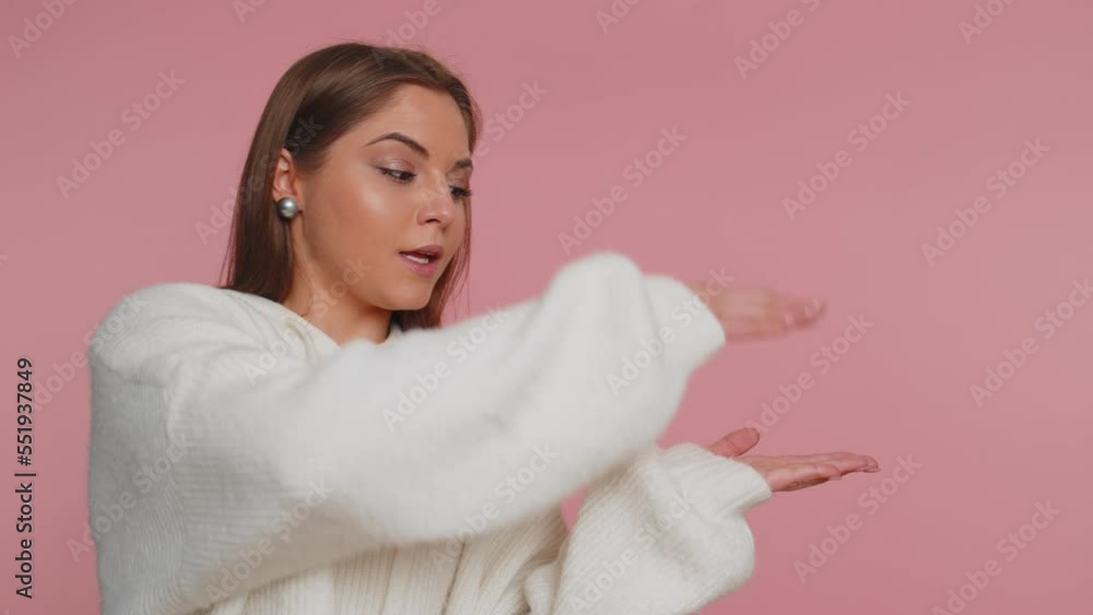 Lovely woman in sweater showing thumbs up and pointing empty place, advertising area for commercial text, copy space for goods promotion. Young adult girl. Indoor studio shot on pink wall background Lovely woman in sweater showing thumbs up and pointing empty place, advertising area for commercial text, copy space for goods promotion. Young adult girl. Indoor studio shot on pink wall background