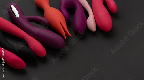 Sex toys and masturbation device. A pink, red, purple and black rubber and silicone dildos is lying on dark paper. View from above. Place for text. Flat lay. Sex shop concept